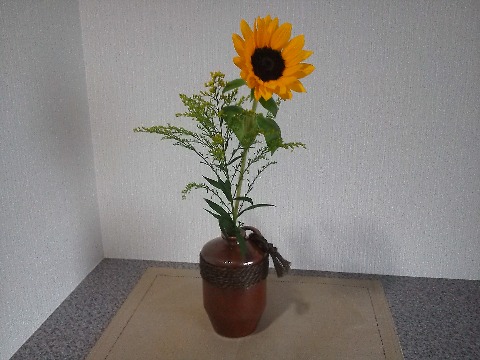 夏至ももう過ぎてしまいましたが，夏はこれからが本番．玄関のお花もひまわりに替わりました．　娘が持ってきてくれたお土産が，中味はとっくにおなかの中ですが，容器がちょっと風流な花器として活躍しています．